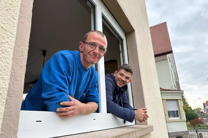 Zwei Monteure von Hollnberger Fensterbau schauen aus einem frisch eingebauten Fenster